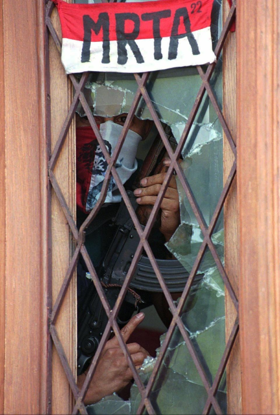 FILE - In this Dec. 31, 1996 file photo, a Tupac Amaru guerrilla watches from the broken glass of the main door of Japan's ambassador residence in Lima, where the guerrillas hold 83 hostages. The rebel group appropriated the name of Tupac Amaru, a muleteer and trader who claimed descent from Inca royals, led an Andean revolt against Spanish colonial rule and was executed on May 18, 1781. (AP Photo/Fernando Llano, File)