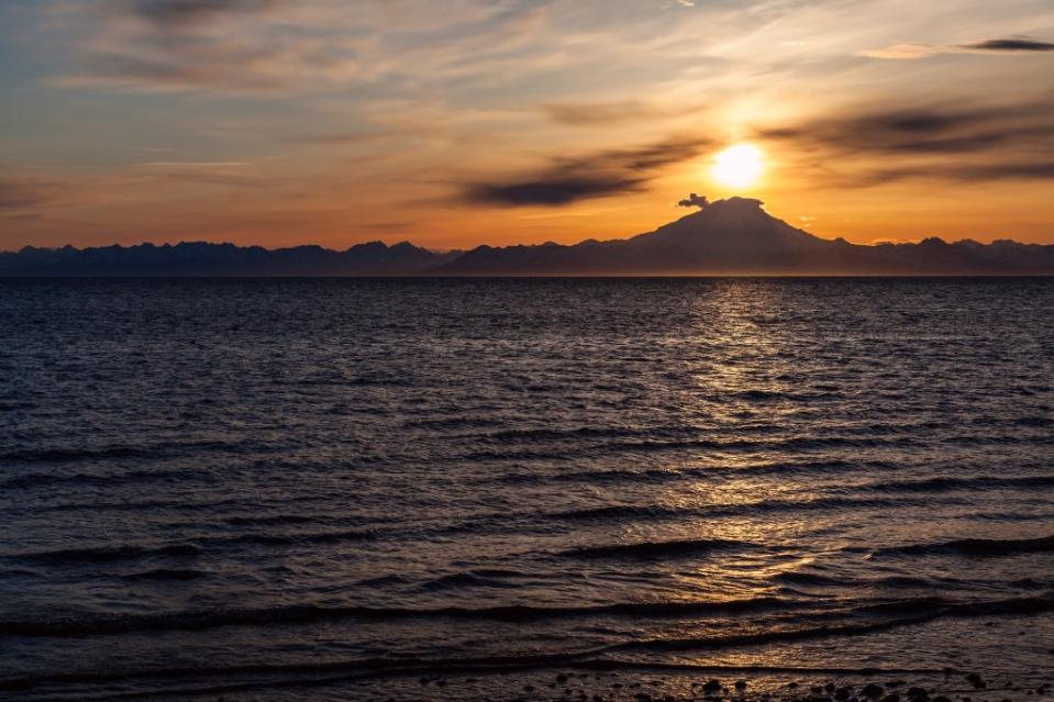 The setting sun crests the summit of the active volcano, Mount Redoubt. Ninilchik, Alaska via Getty Images