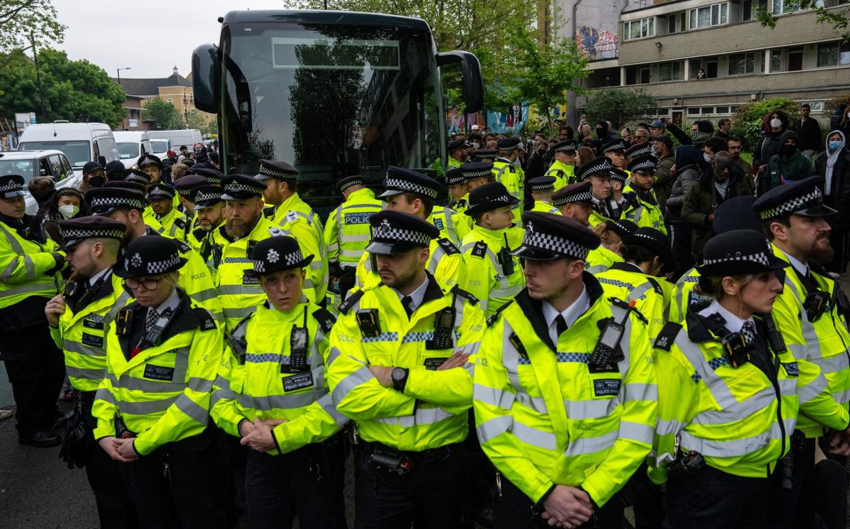 Police officers surround a bus that was to be used to carry migrants from a hotel in Peckham