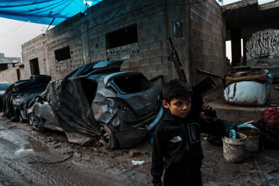 A young boy plays along a street filled with detritus of cars.