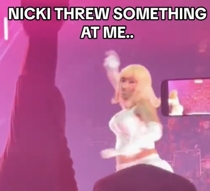 Nicki Minaj on stage throwing an object, audience in foreground, text overlay: "NICKI THREW SOMETHING AT ME.."