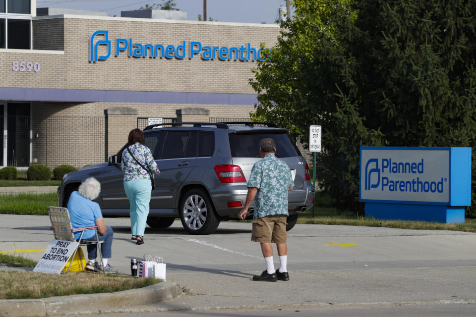 FILE - Abortion protesters attempt to hand out literature at a Planned Parenthood clinic in Indianapolis, on Aug. 16, 2019. Planned Parenthood is shifting funding to its state affiliates and cutting national office staff to reflect a changed landscape in both how abortion is provided and how battles over access are playing out. The group, a major provider of abortion and other health services and also an advocate for abortion access, told its staff on Monday, May 22, 2023, that layoff notices would go out in June and provided The Associated Press with an overview Tuesday. (AP Photo/Michael Conroy, File)