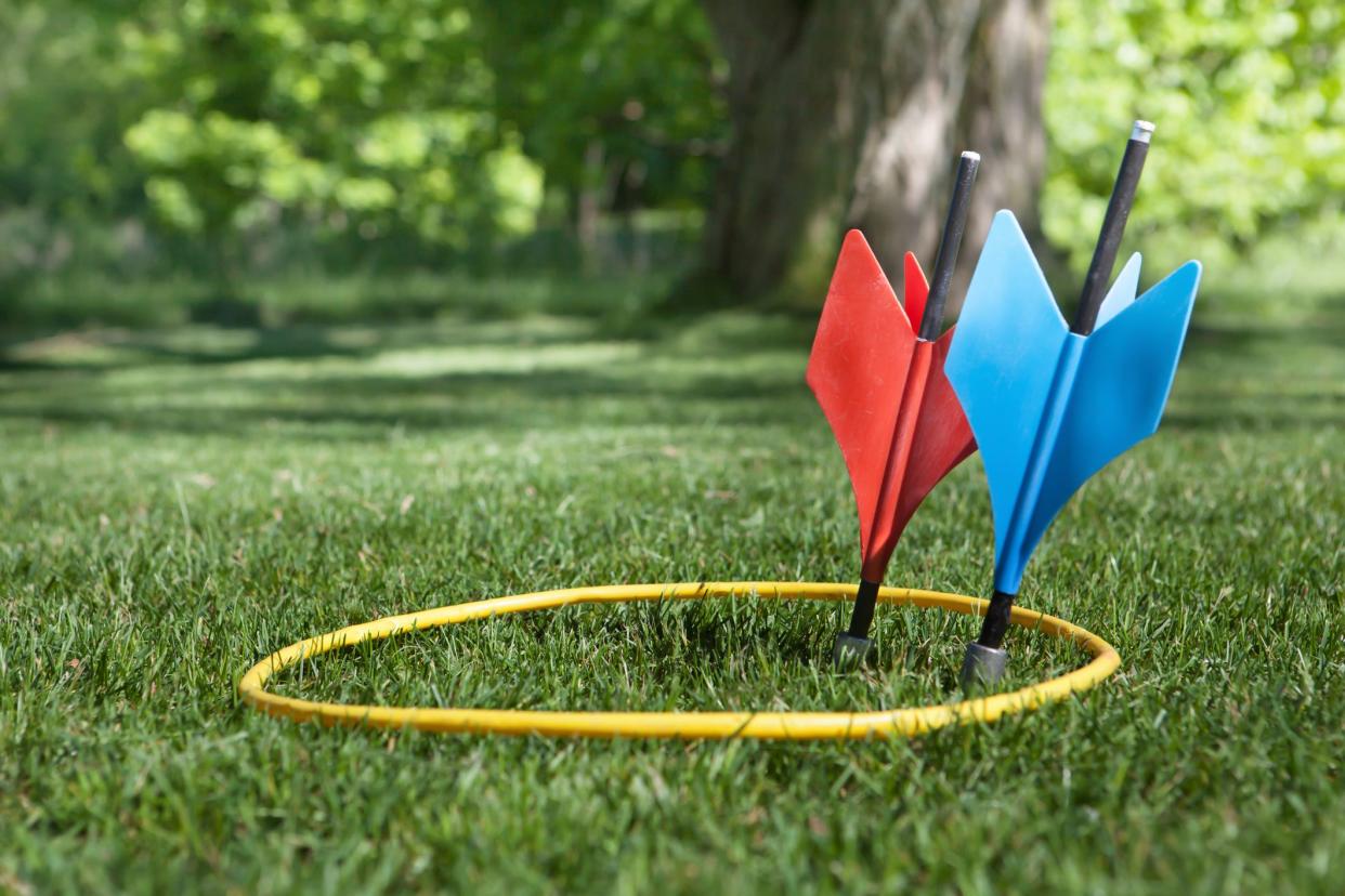 a shot of some vintage lawn darts somtimes called JARTS. One of each  color inside the yellow ring in a back yard setting.