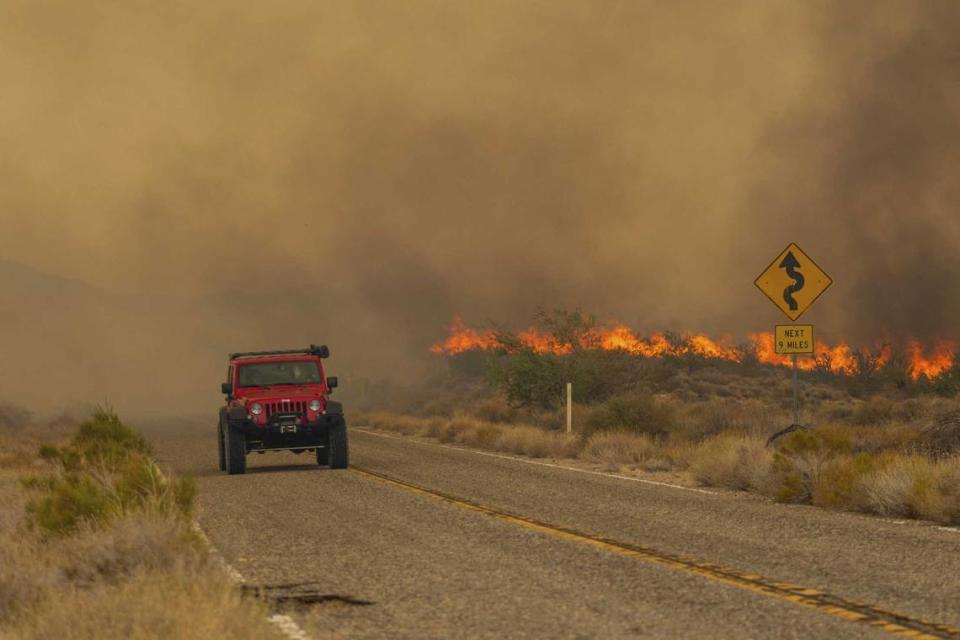 A car passes rising flames from the York Fire on Sunday in the Mojave National Preserve. Crews battled “fire whirls” as a the state’s largest wildfire of 2023 crossed into Nevada amid dangerously high temperatures and raging winds.