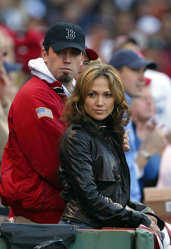 He's wearing a Boston Red Sox cap and standing with JLo