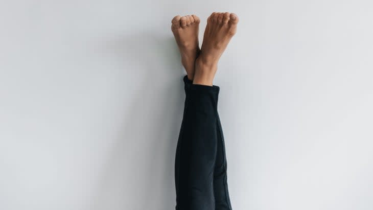 Person practices legs up the wall with legs crossed against a white wall