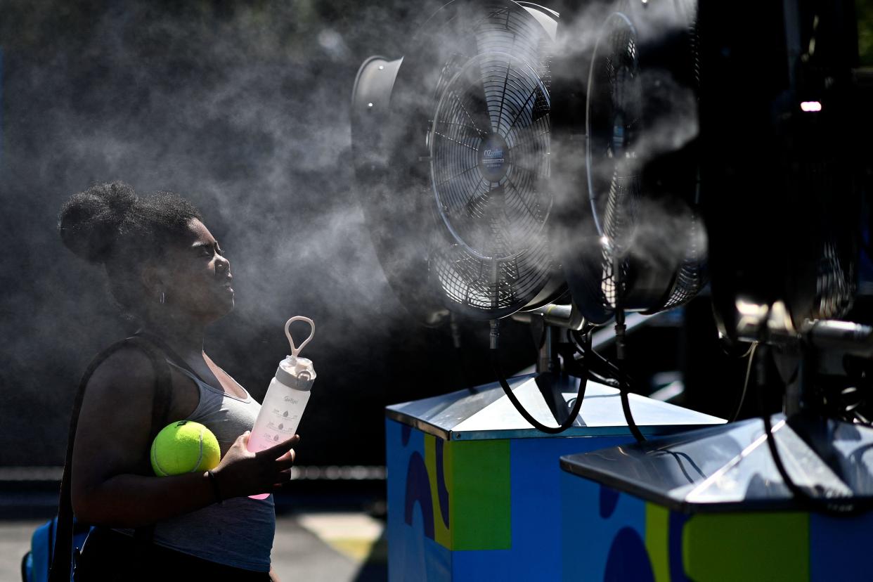 A woman cools off from the heat in front of mist cooling fans at the Melbourne Park ahead of the Australian Open tennis tournament in Melbourne on January 14, 2023.&nbsp; / Credit: MANAN VATSYAYANA/AFP via Getty Images