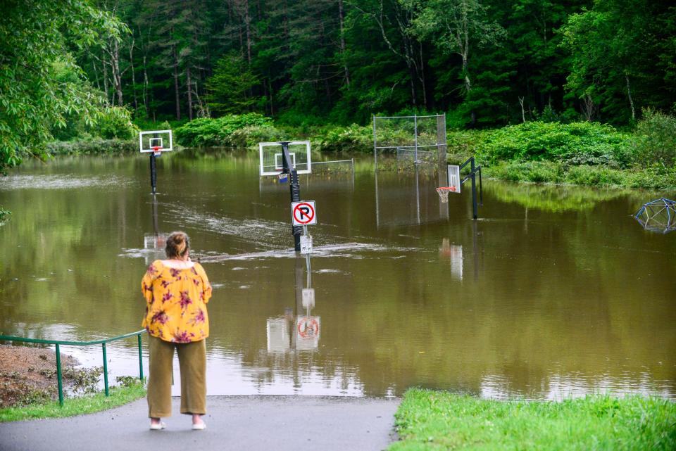 Karen Matter, of Amherst, N.H., takes a video of the flooding from the North Branch Deerfield River in Wilmington, Vt., on Monday, July 10, 2023. Heavy rain has washed out roads and forced evacuations in the Northeast, especially in Vermont and New York. (Kristopher Radder/The Brattleboro Reformer via AP)