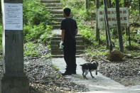 A worker with a dog looks up on a path into the hillside as a search for a runaway leopard suspected to be in the area in Hangzhou in eastern China's Zhejiang province Sunday, May 9, 2021. A search for the last of three leopards that escaped from a safari park in eastern China was ongoing, authorities said Monday, May 10, 2021 as the park came under fire for concealing the breakout for nearly a week. (Chinatopix via AP)