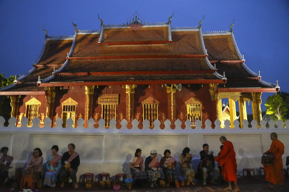 People offer food to Buddhist monks outside Sensoukharam temple in Luang Prabang, Laos, Sunday, Jan. 28, 2024. Luang Prabang was named a UNESCO World Heritage Site nearly 30 years ago, but a multibillion-dollar dam project is raising questions that could deprive the city of its coveted status and prompting broader concerns the Mekong River could be ruined by multiple dams that are being planned.(AP Photo/Sakchai Lalit)