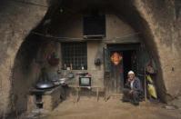 Un hombre fuma sentado<b> en la entrada de su casa-cueva en Yuncheng</b>, China. (REUTERS/China Daily).