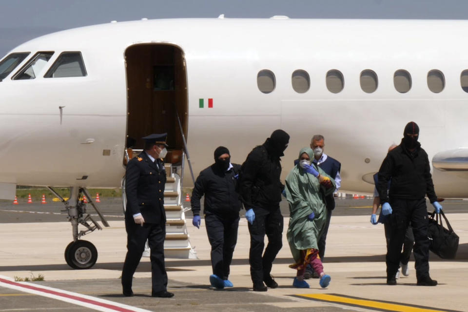 In this image taken from a video, Silvia Romano walks on the tarmac after landing at Rome's Ciampino airport, Sunday, May 10, 2020. Wearing a surgical mask, disposable gloves and booties to guard against COVID-19, a young Italian woman has returned to her homeland after 18 months as a hostage in eastern Africa. (AP Photo/Paolo Santalucia)