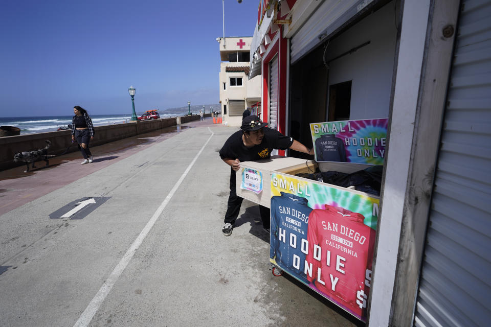 Noe Reyes closes up a stand that sells hoodies along a beachfront promenade after heavy rain was forecast for the afternoon, Tuesday, March 21, 2023, in San Diego. Californians are tired. Tired of the rain, tired of the snow, tired of stormy weather and the cold, relentlessly gray skies that have clouded the Golden State nearly nonstop since late December. (AP Photo/Gregory Bull)