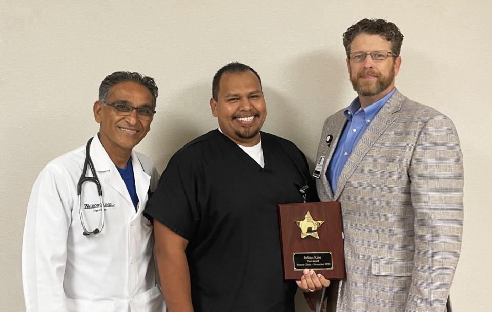 Julian Rios, R.N., center, holds his PEER Award plaque. Also pictured are Watson Clinic Chief Administrative Officer Jason Hirsbrunner, right, and Watson Clinic Urgent Care Main specialist Dr. Rajendra K. Sawh, left.