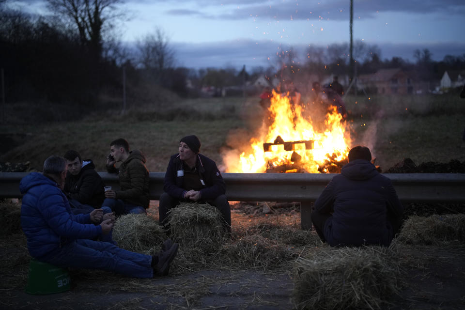 Farmers relax by a bonfire as they block a highway Tuesday, Jan. 30, 2024 in Jossigny, east of Paris. With protesting farmers camped out at barricades around Paris, France's government hoped to calm their anger with more concessions Tuesday to their complaints that growing and rearing food has become too difficult and not sufficiently lucrative. (AP Photo/Christophe Ena)