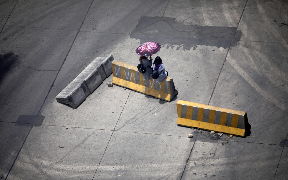 Women sit on at traffic barrier, one of many used by supporters of former President Evo Morales to block a highway in El Alto, Bolivia, Nov. 16, 2019. (AP Photo/Natacha Pisarenko)