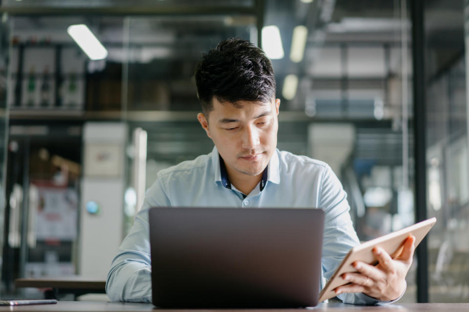 a person sitting at their computer and looking at a tablet