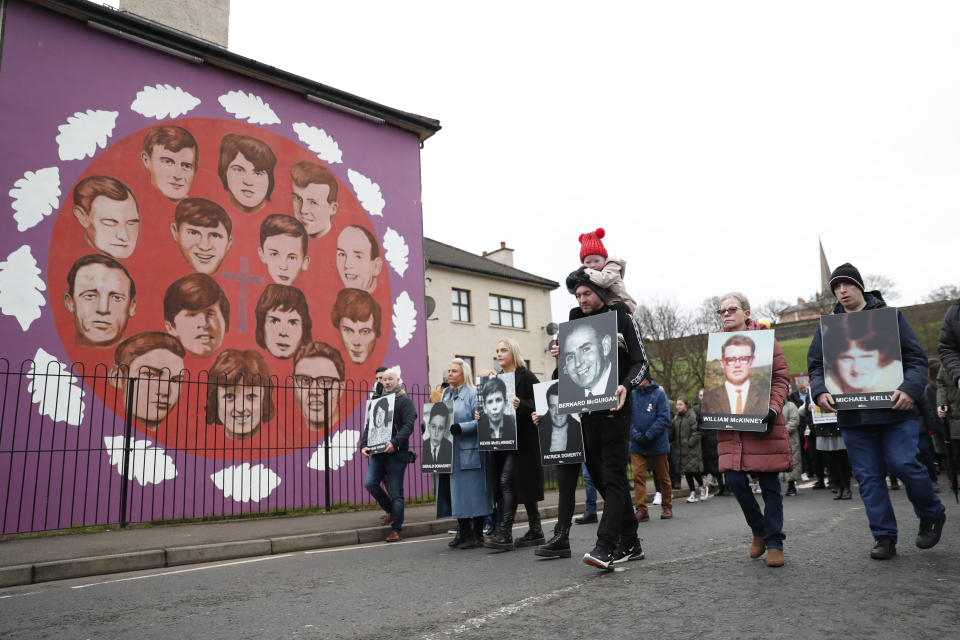People take part in a march to commemorate the 50th anniversary of the 'Bloody Sunday' shootings, holding photographs of some of the victims, as they pass a mural dedicated to those who died, in Londonderry, Sunday, Jan. 30, 2022. In 1972 British soldiers shot 28 unarmed civilians at a civil rights march, killing 13 on what is known as Bloody Sunday or the Bogside Massacre. Sunday marks the 50th anniversary of the shootings in the Bogside area of Londonderry .(AP Photo/Peter Morrison)
