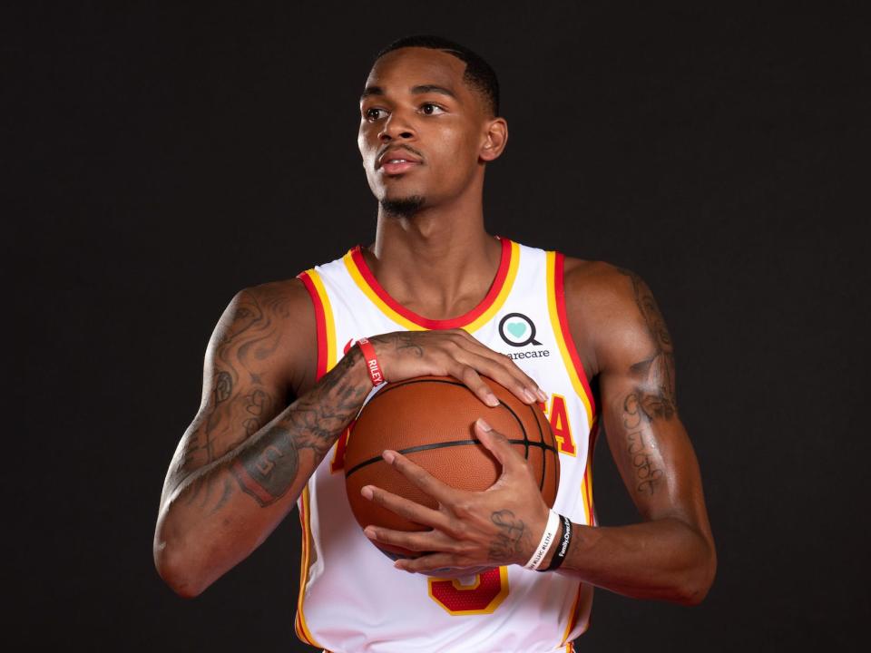 Dejounte Murray holds a basketball and looks off to the side in a Hawks jersey during a photoshoot.