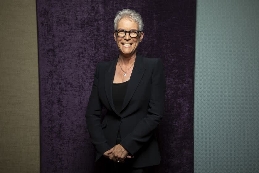 A woman in a black suit smiles while posing formally in front of a backdrop