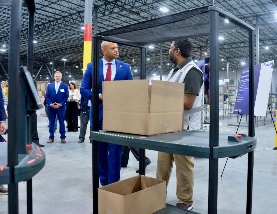 A worker at the new Conair distribution center near Hagerstown explains to Gov. Wes Moore how Cobots or collaborative robots assist employees. The Cobots look like double-stacked audiovisual carts.