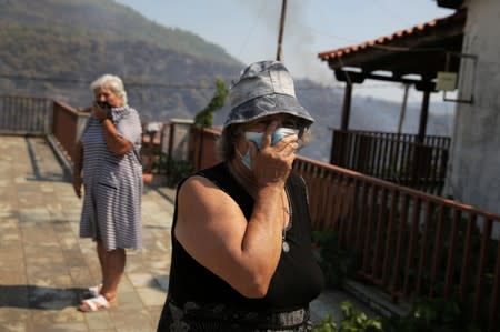 A woman covers her face to avoid inhaling smoke as a wildfire burns in the village of Makrimalli on the island of Evia