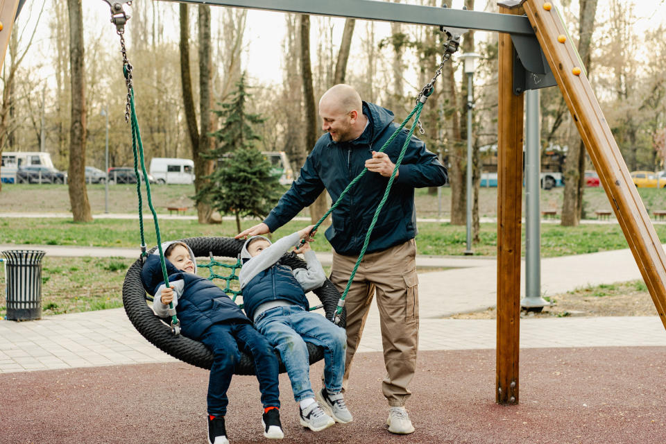 Adult swings two children on a large nest swing at a park. They are having fun