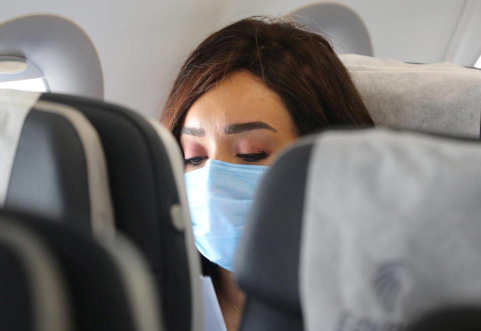 A young woman passenger in a surgical mask seated on a plane. 