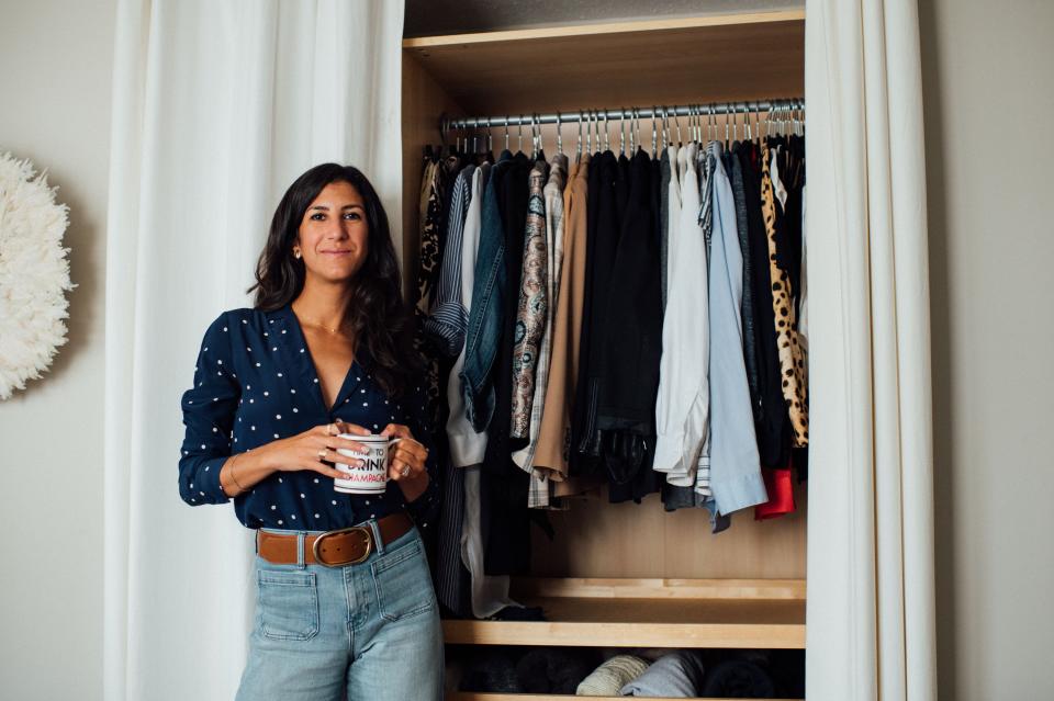 Sustainable stylist Alyssa Beltempo wears a polka dot blouse and jeans in front of an open closet