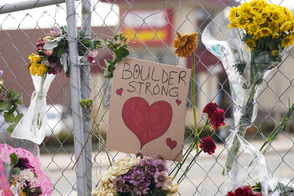 A sign is flanked by floral bouquets placed on the temporary fence put up around the parking lot of a King Soopers grocery store Thursday, March 25, 2021, in Boulder, Colo. Ten people were killed in a mass shooting at the supermarket on Monday. (AP Photo/David Zalubowski)