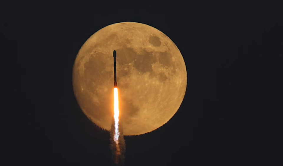 Space X Falcon 9 rocket flies past a full moon.