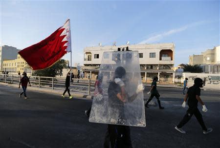 An anti-government protester walks with a glass pane for protection, as another waving a Bahrain national flag marches towards riot police, during clashes after a revisit to the grave of detainee Jaffar Mohammed Jaffar, in the village of Daih west of Manama, March 3, 2014. REUTERS/Hamad I Mohammed