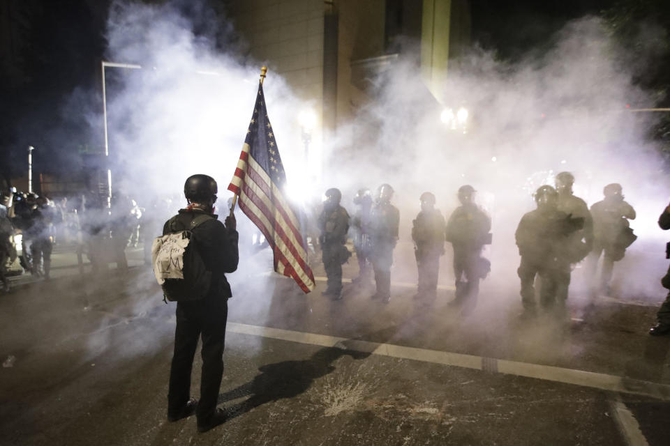 A demonstrator waves a U.S. flags in front of federal agents after tear gas is deployed during a Black Lives Matter protest at the Mark O. Hatfield United States Courthouse early on July 30, 2020, in Portland, Oregon. / Credit: Marcio Jose Sanchez / AP