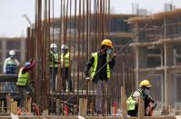 Workers wearing protective face masks stand on a building under construction in the New Administrative Capital (NAC), east of Cairo