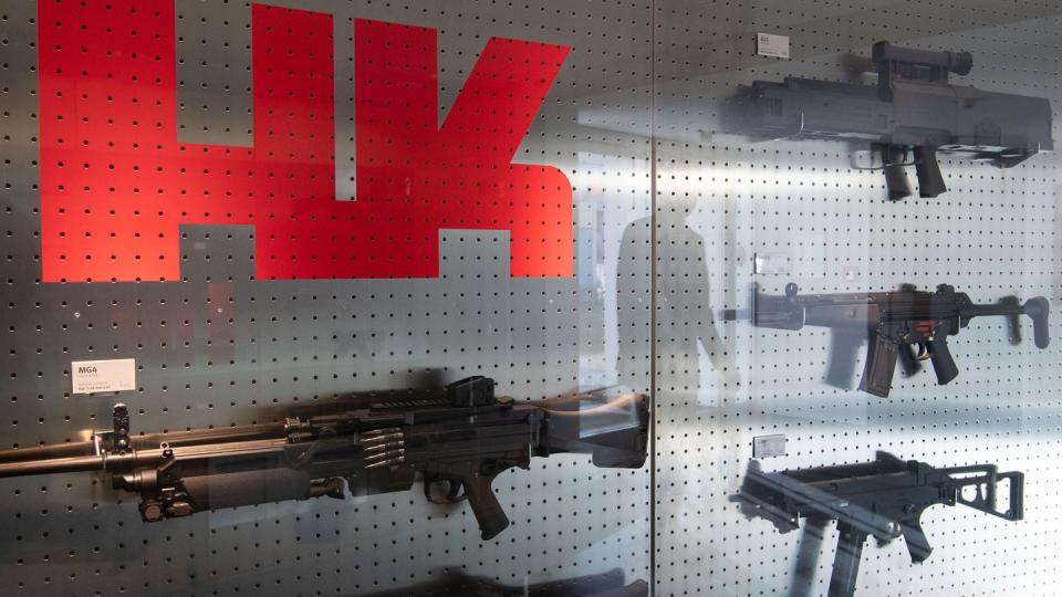 Das Logo des Waffenherstellers Heckler & Koch ist auf dem Firmengelände an einer Präsentationswand neben Waffen zu sehen.