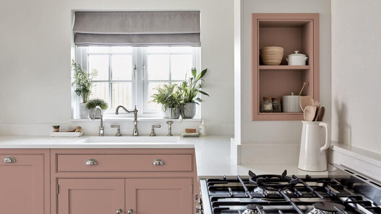  A pink and white kitchen with sink beneath window and gas burner stove 