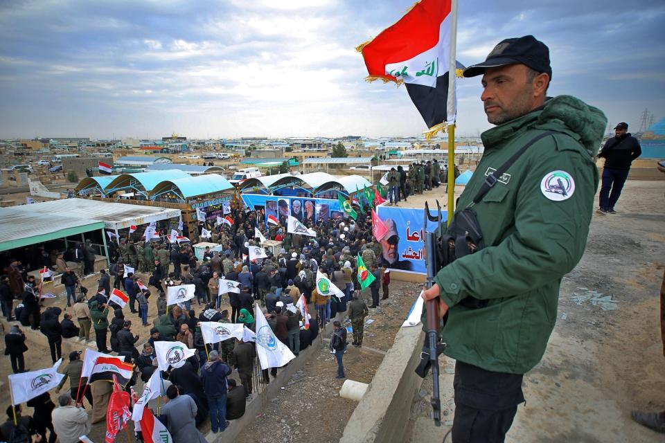 An armed guard stands over mourners and family members as they prepare to bury the body of Abu Mahdi al-Muhandis, deputy commander of Iran-backed militias who was killed in a US airstrike in Iraq on Friday, in Wadi al-Salam, or "Valley of Peace" cemetery, during his funeral procession in Najaf, Iraq, Wednesday, Jan. 8, 2020. (AP Photo/Anmar Khalil)