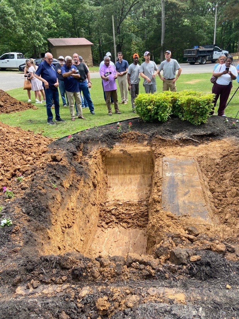 Onlookers look down as City of Jackson workers wait for equipment to help uncover the time capsule at Muse Park on Wednesday, June 1, 2022.