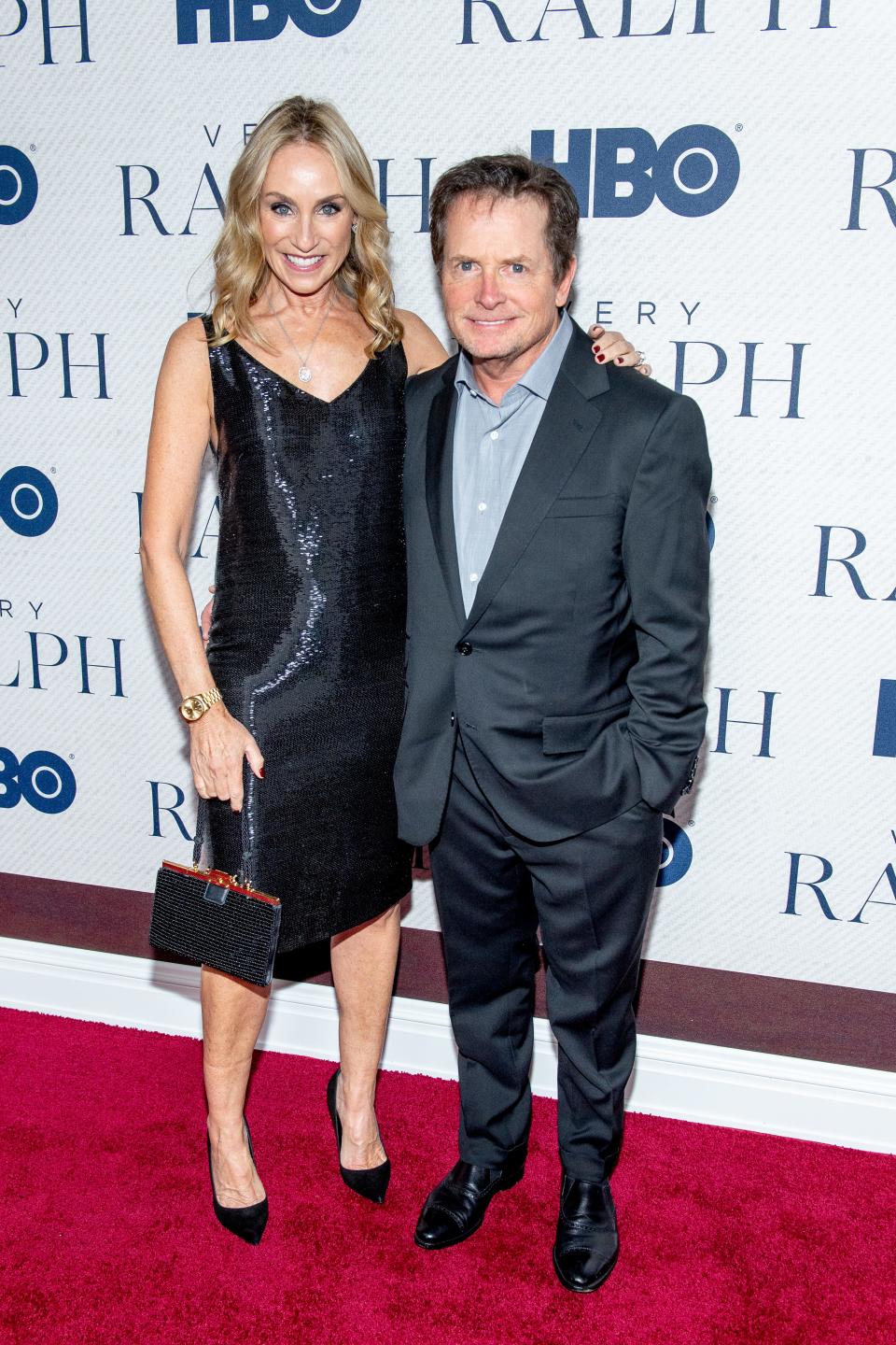 Tracy Pollan in a sparkling dark blue knee-length dress and heels standing taller than Michael J. Fox in a grey suit.