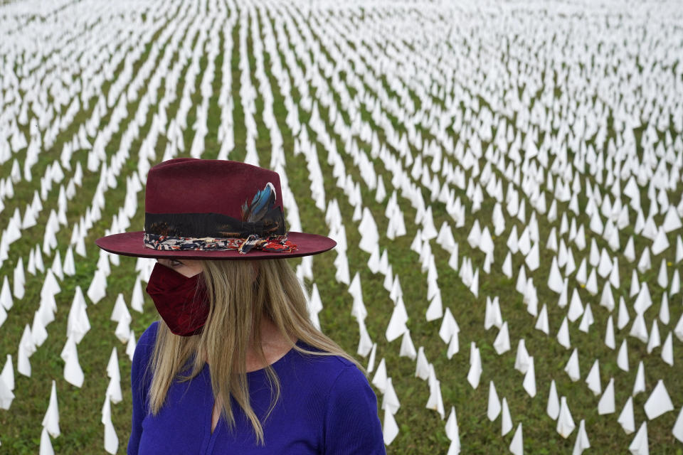 Artist Suzanne Brennan Firstenberg stands among thousands of white flags planted in remembrance of Americans who have died of COVID-19, Tuesday, Oct. 27, 2020, near Robert F. Kennedy Memorial Stadium in Washington. Firstenberg's temporary art installation, called "In America, How Could This Happen," will include an estimated 240,000 flags when completed. (AP Photo/Patrick Semansky)