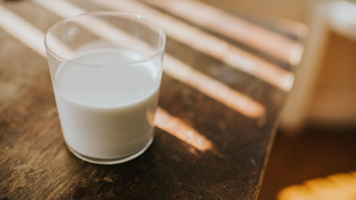  A glass of milk sitting on a wooden table. 