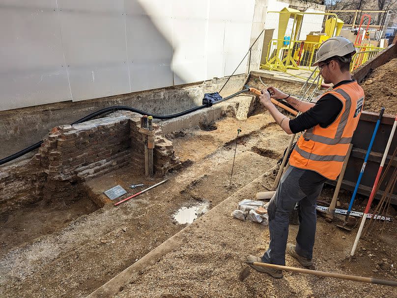 An archaeologist takes a photo of part of the excavation, including a fragment of the post-Medieval wall.