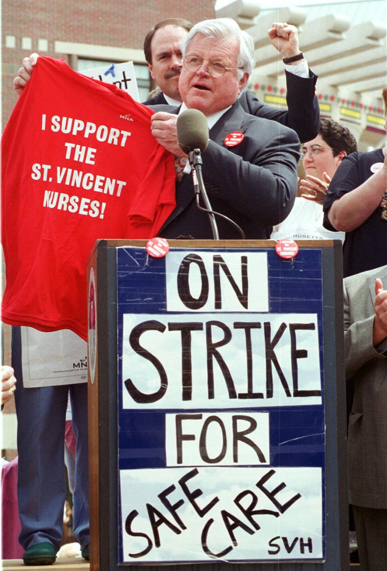 U.S. Sen. Edward M. Kennedy, D-Mass., holds up a T-shirt on Friday, May 5, 2000, in support of striking nurses in Worcester. Kennedy attended the afternoon rally to show his support for the nurses, who are striking over the issue of mandatory overtime. Worcester Mayor Raymond V. Mariano is seen in the background with a raised fist.