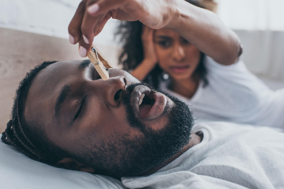 Woman pinning man's noise as he snores next to her in bed. (Getty Images)