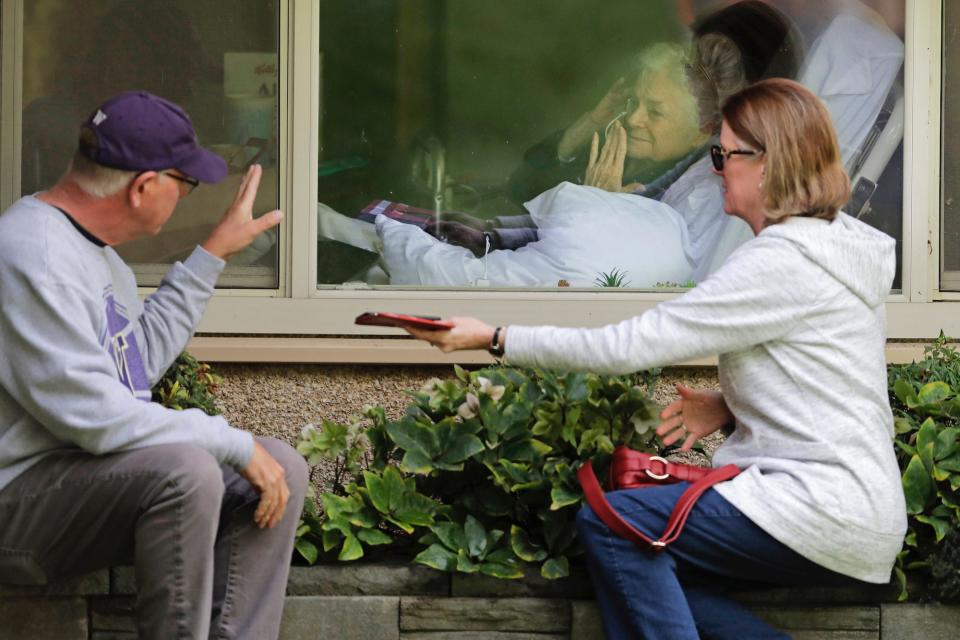 Judie Shape, center, who has tested positive for the coronavirus, blows a kiss to her son-in-law, Michael Spencer, left, as Shape's daughter, Lori Spencer, right, looks on, Wednesday, March 11, 2020, as they visit on the phone and look at each other through a window at the Life Care Center in Kirkland, Wash., near Seattle.