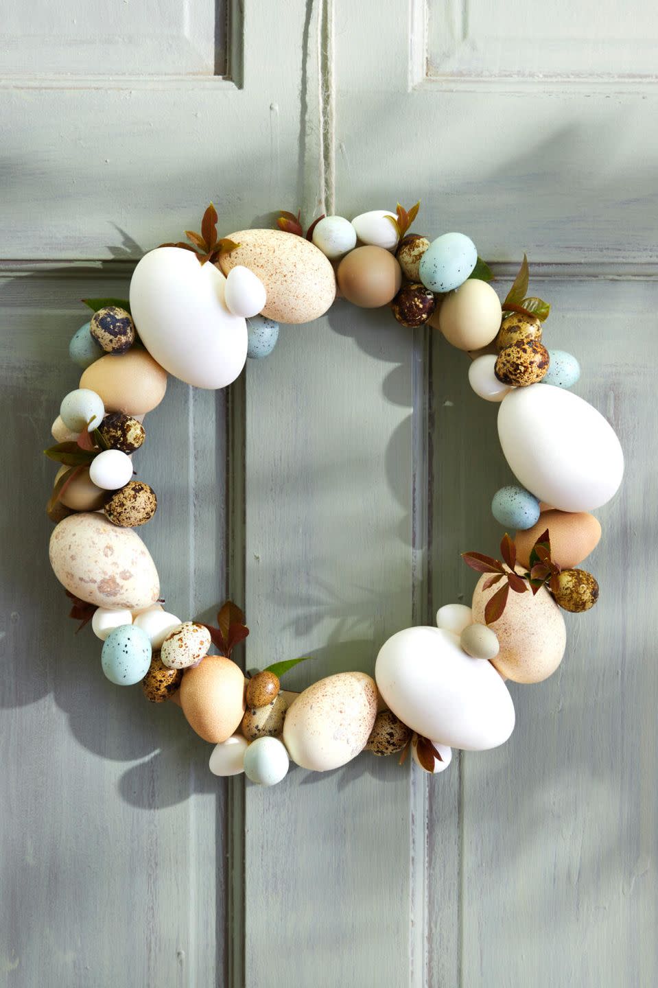 a wreath made from different color, shape, and size eggs hung on a blue door