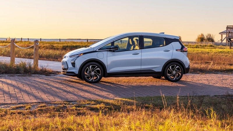 A Chevrolet Bolt parked on a brick driveway with a wetland landscape in the background. The sun is setting, casting long shadows from the grasses and reeds. 