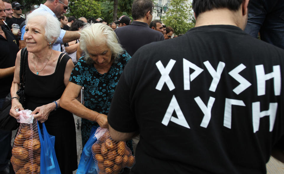 Elderly women receive potatoes as a member of Greece's extreme right Golden Dawn with T-shirt of his party party stands at Athens' main Syntagma Square, opposite parliament, on Wednesday, Aug. 1, 2012. The volunteers checked ID cards of the public before handing Greek citizens food that included milk cartons, pasta, potatoes and olive oil. Golden Dawn won 18 seats in the 300-seat parliament in June general elections. Senior party members openly support a policy of granting Greek citizenship based on racial identity. The party has stepped up its charity effort as Greece is suffering through a fifth year of recession, with rapidly rising rates of poverty and unemployment. (AP Photo/Thanassis Stavrakis)