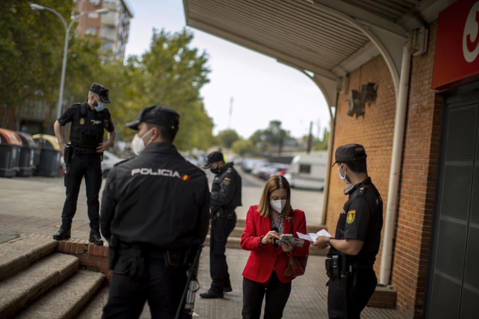 Police officers speak to people at a checkpoint at Orcasitas station in the Orcasitas neighbourhood in Madrid, Spain, Tuesday, Sept. 29, 2020. Spain's health minister has pleaded for the third time in four days for tougher measures in the capital. The national government wants to see existing restrictions against the spread of the virus extended to the entire city while regional officials say that time is needed to see if the current limitations have an effect and that drastic measures would further hurt Spain's economy. (AP Photo/Manu Fernandez)