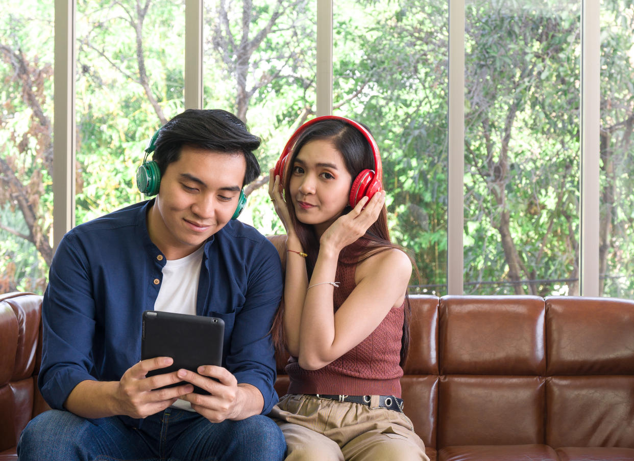 Young lovers spend time together on holidays in the living room. Both are interested in music from headphones while the man holding tablet computer.